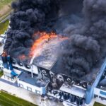 Aerial view of burnt industrial warehouse or logistics center building after big fire with huge smoke from burned roof